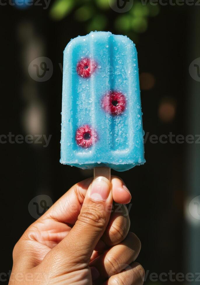 A close up of a refreshing blue popsicle with raspberries held by a hand. photo