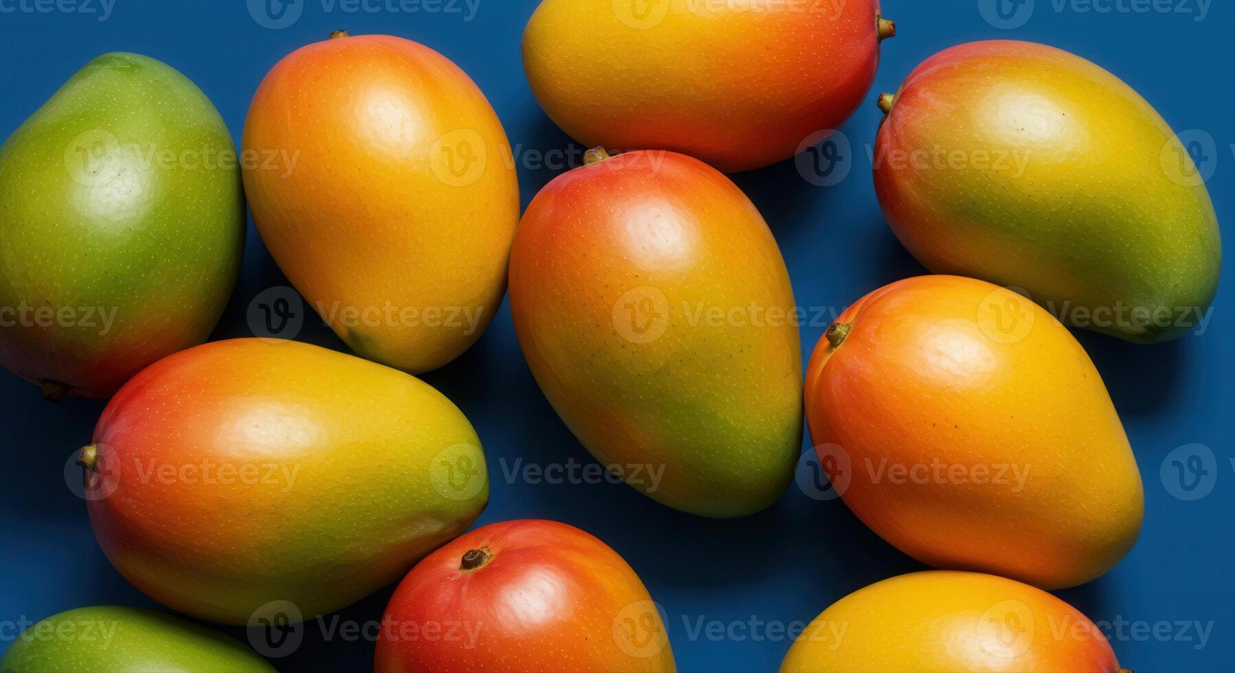 A close up shot of various ripe and colorful mangoes arranged on a blue surface. photo