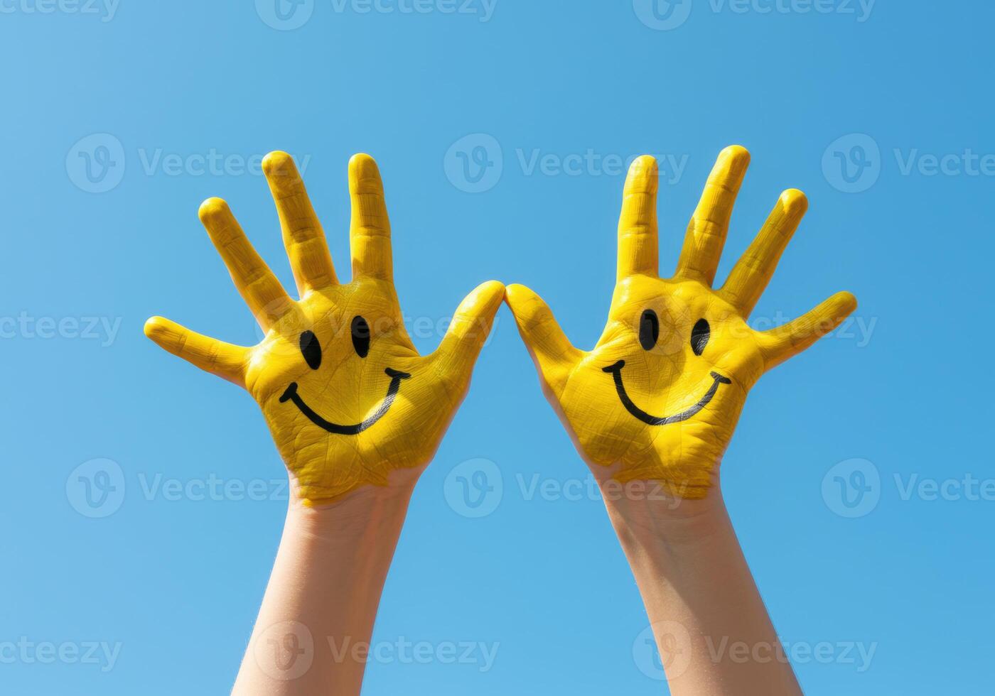 Two hands raised with painted smiley faces against a bright blue sky. photo