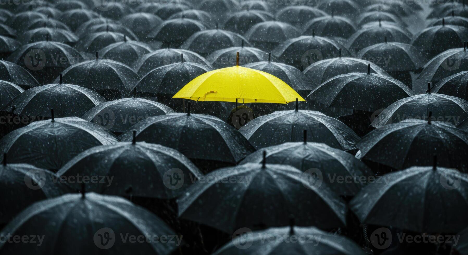 A single vibrant yellow umbrella pops against a backdrop of many dark umbrellas in the rain. photo