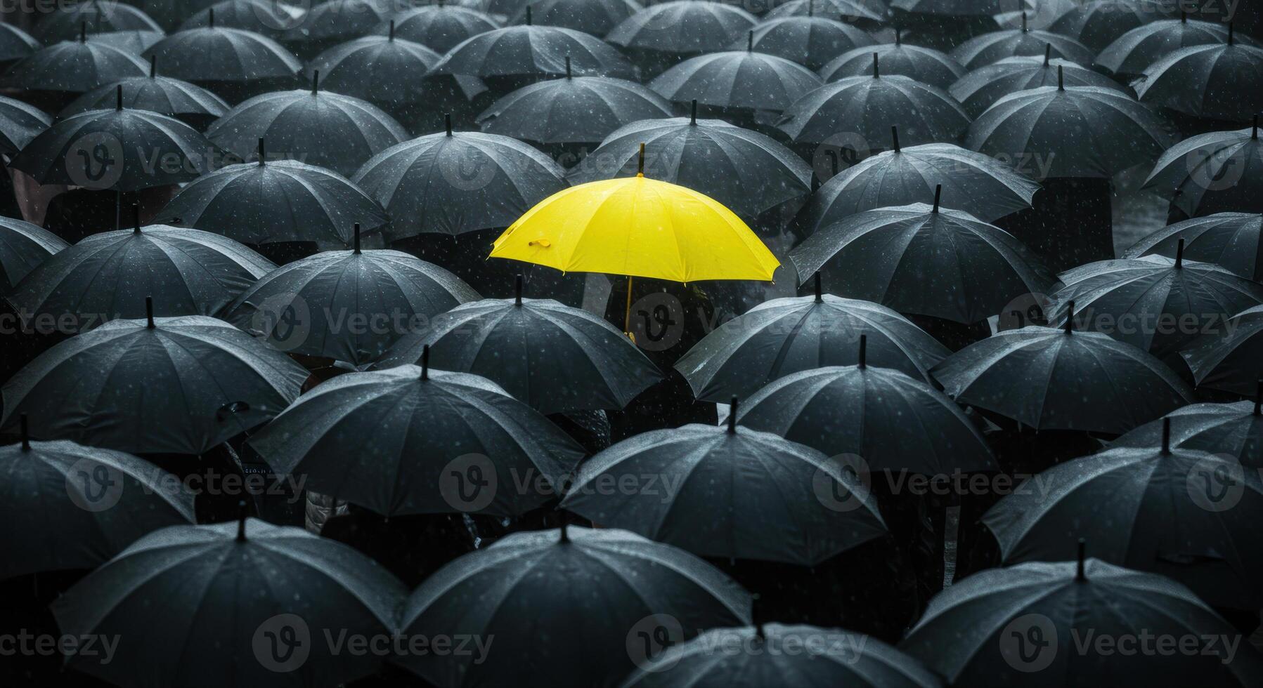 A vibrant yellow umbrella stands out from a sea of black umbrellas in the rain. photo