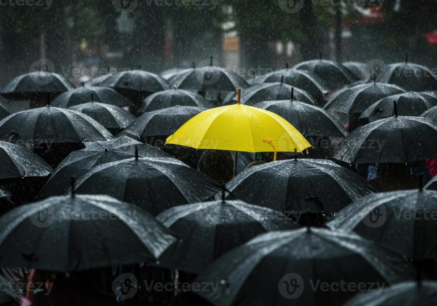 A yellow umbrella pops against a backdrop of black umbrellas in a rainy scene. photo