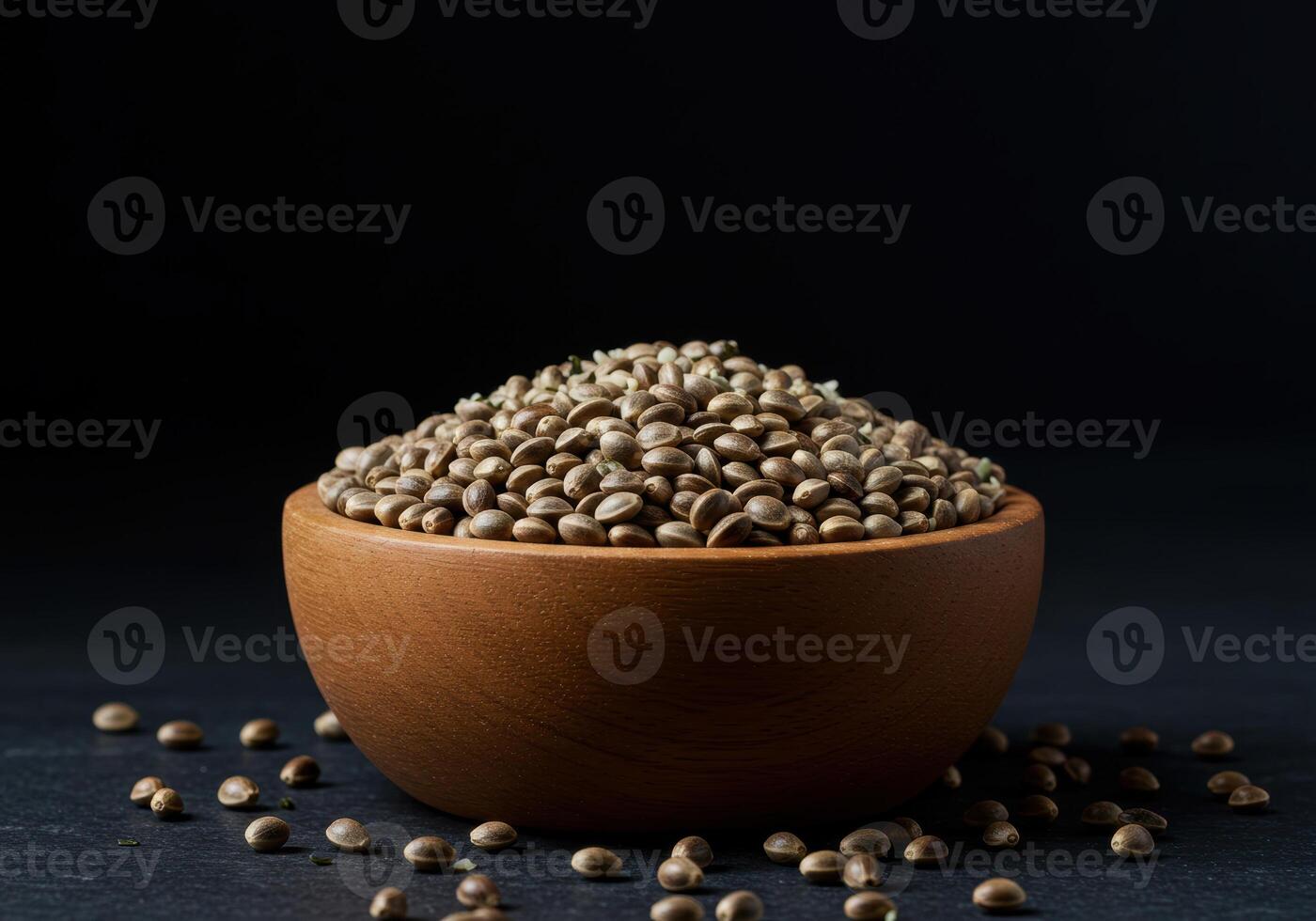 A wooden bowl filled with hemp seeds is placed on a dark, textured surface. photo