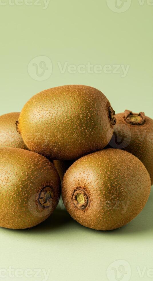 A collection of fresh ripe kiwis stacked against a solid soft green backdrop. photo