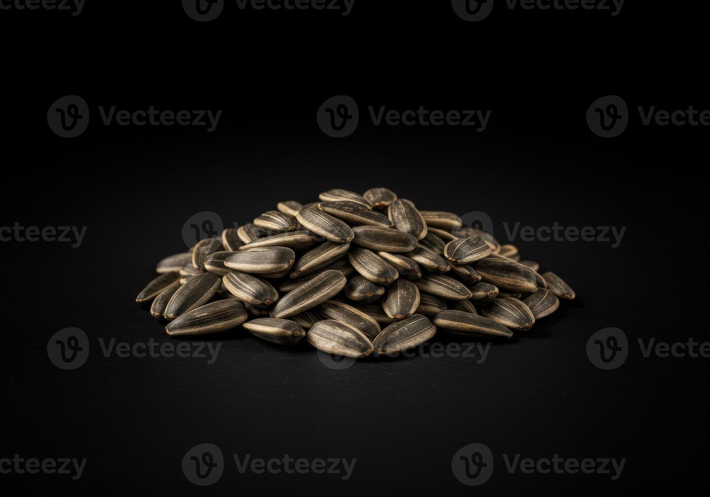 A collection of sunflower seeds arranged in a small pile, against a deep black backdrop. photo