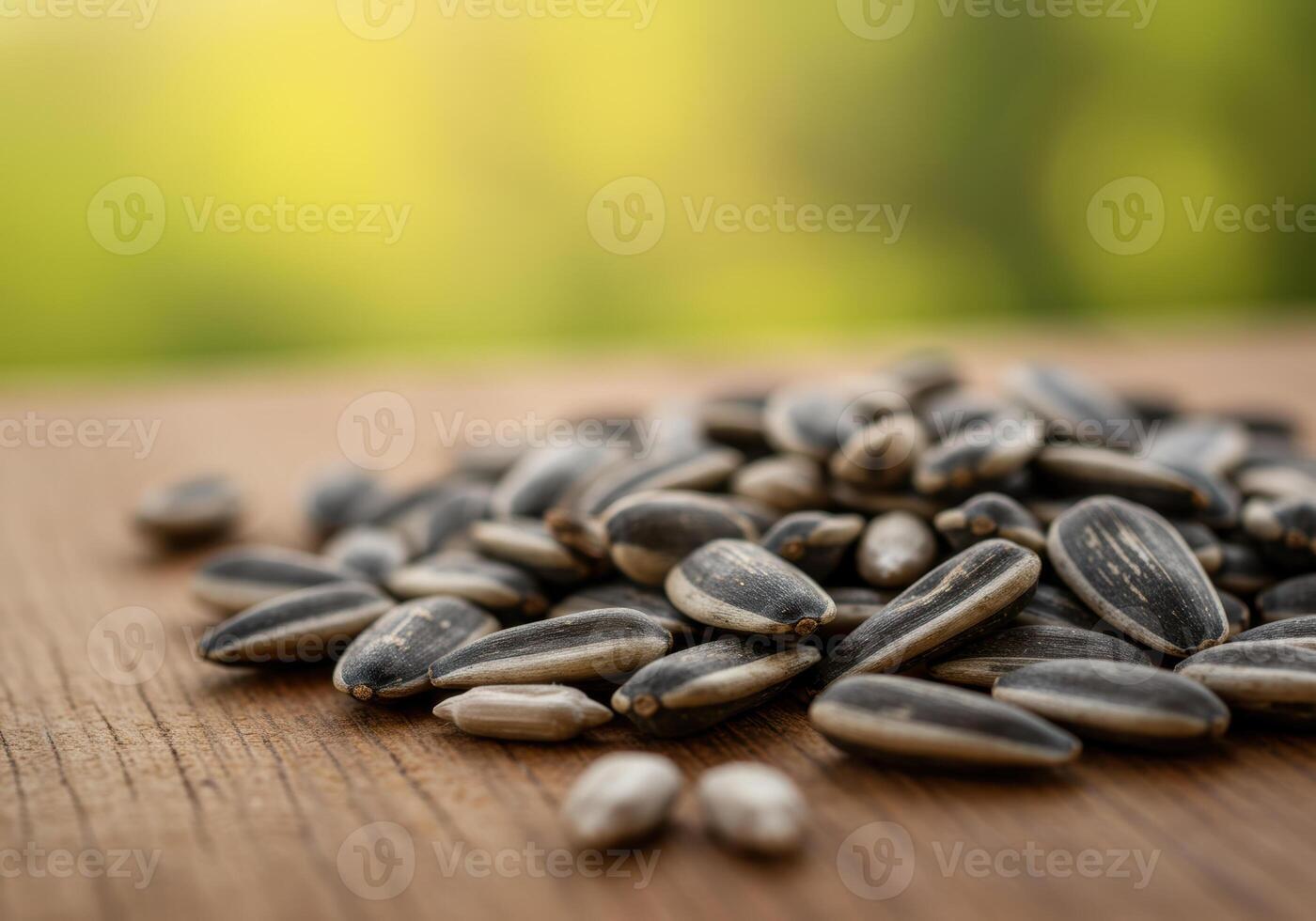 A mound of sunflower seeds rests on a wooden surface with a green background. photo