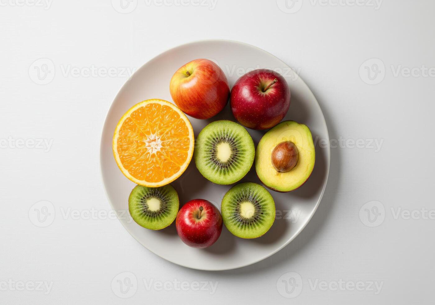 An assortment of fresh fruits, including apples, kiwis, orange, and avocado, on a white plate. photo