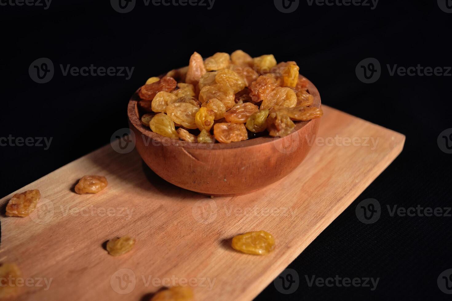 High angle view of a bowl of raisins on a wooden cutting board with a dark background. Food photography of a bunch of dried grapes commonly used in cooking and baking. photo