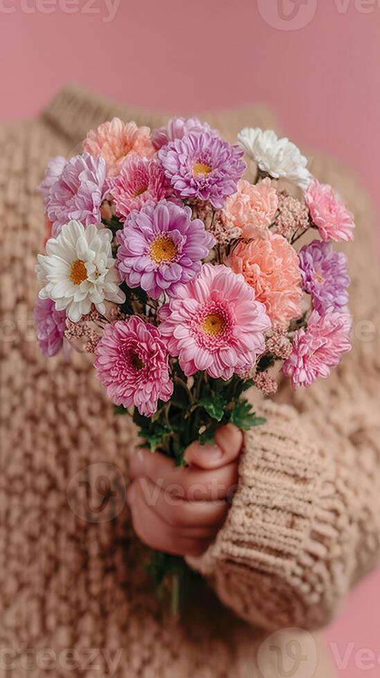 Colorful bouquet of flowers held by a person in a cozy sweater against a pastel backdrop photo