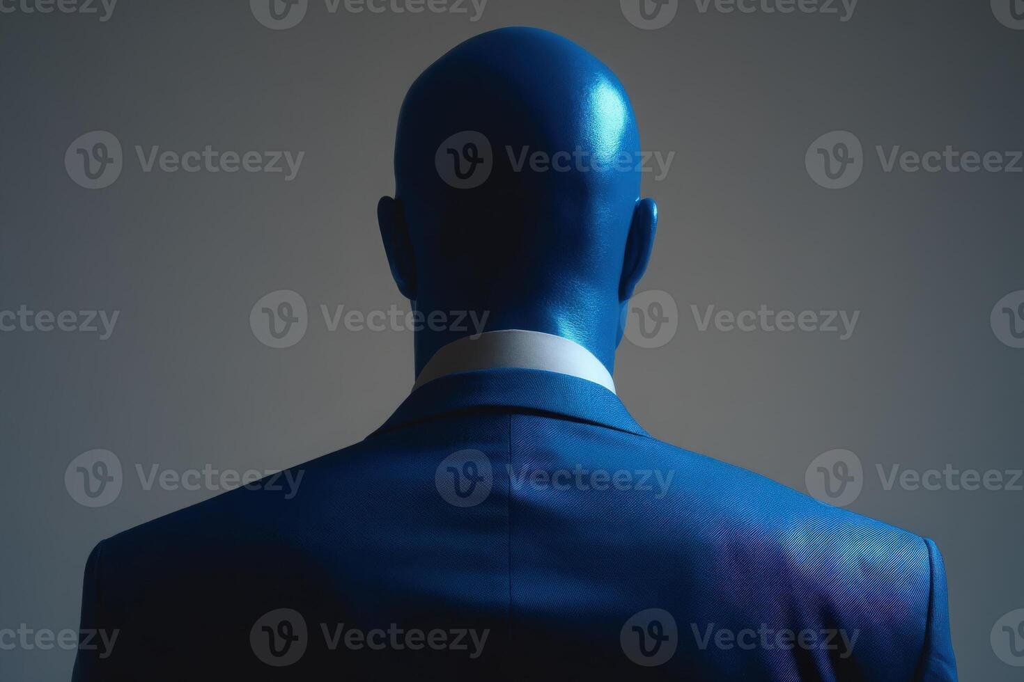 A well-dressed individual with a bald head is seen from behind, wearing a tailored dark suit. The focus is on the sleek silhouette against a softly lit, neutral backdrop. photo