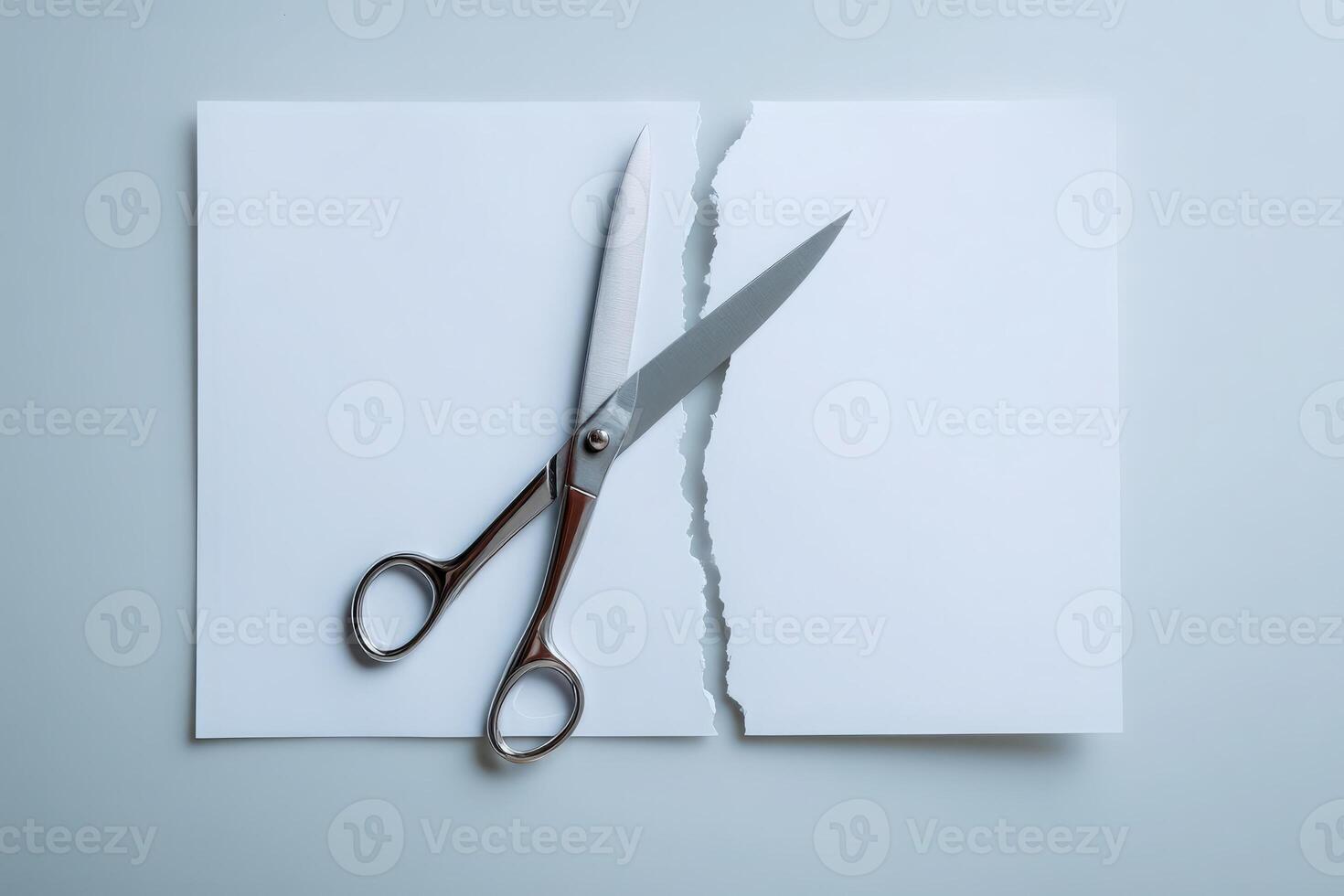 Scissors rest on a partially torn sheet of plain white paper on a clean surface, highlighting the act of cutting. The simple setup creates a focus on creativity and art. photo