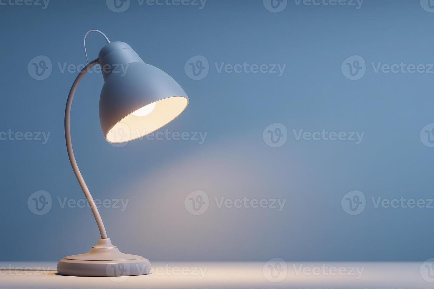 A modern desk lamp with a curved neck is illuminating a small area with warm light. The soft blue background adds tranquility, creating a cozy ambiance perfect for reading or working. photo