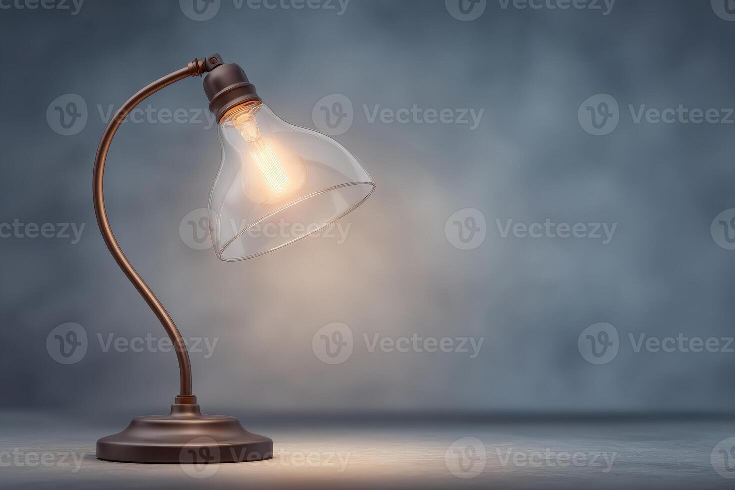 A vintage-style lamp with a clear glass shade emits a warm glow, casting soft light on a textured background. The lamps elegant curve adds charm to the inviting atmosphere. photo