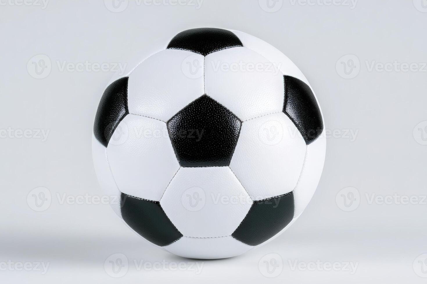 A white soccer ball with black pentagon patches is prominently displayed against a plain background. The focus is on the balls texture and classic design, showing detailed stitching. photo