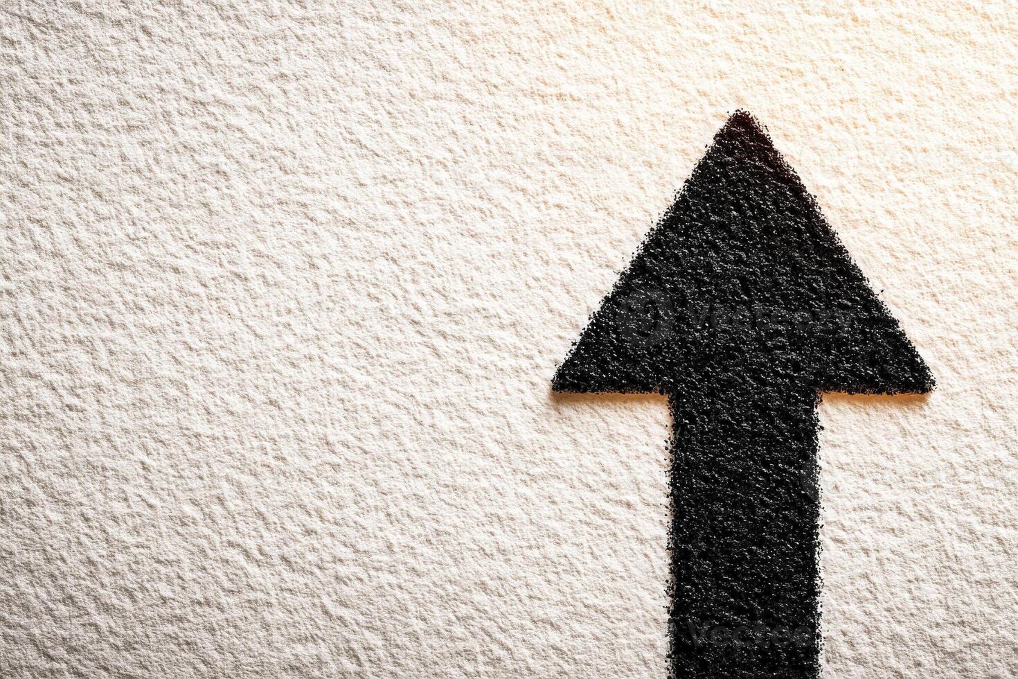 A bold black arrow is displayed prominently on a textured white surface, emphasizing direction and movement. The stark contrast creates a striking visual impact. photo