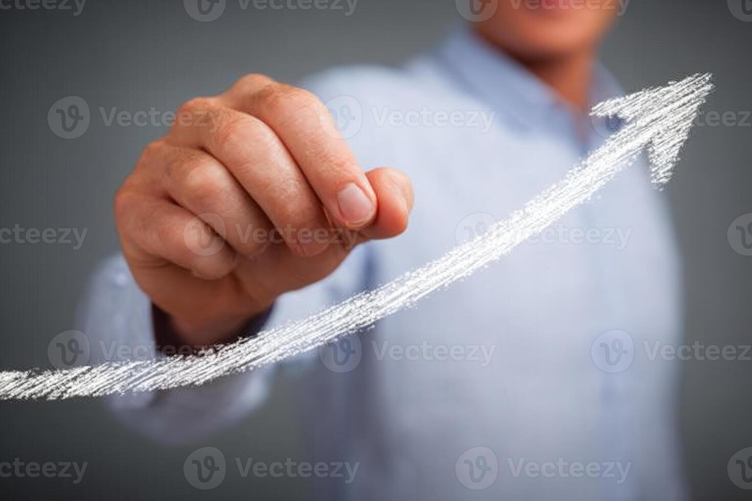 A business professional in a light blue shirt draws an upward arrow using chalk on a gray background, symbolizing growth and success in a business context. photo