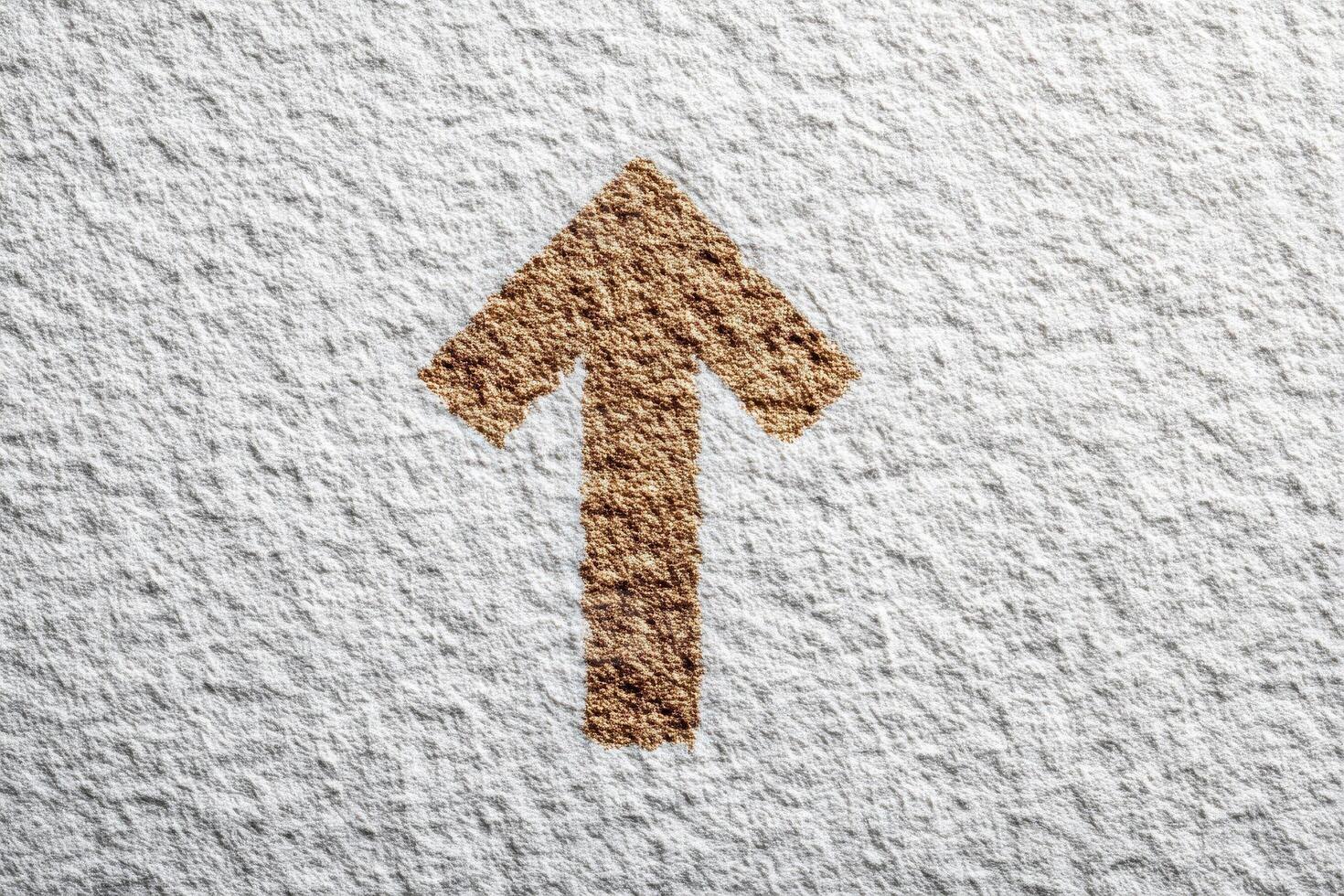 A tan arrow points upward. The arrow and background surface have a rough, textured appearance. The arrows color contrasts with the white, uneven surface. photo