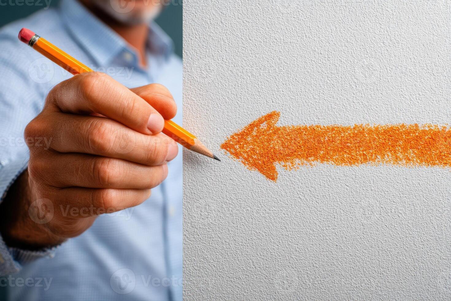 A hand holds a yellow pencil, illustrating the act of drawing an orange arrow on a textured white surface. The environment appears well-lit, focusing on the creative process. photo