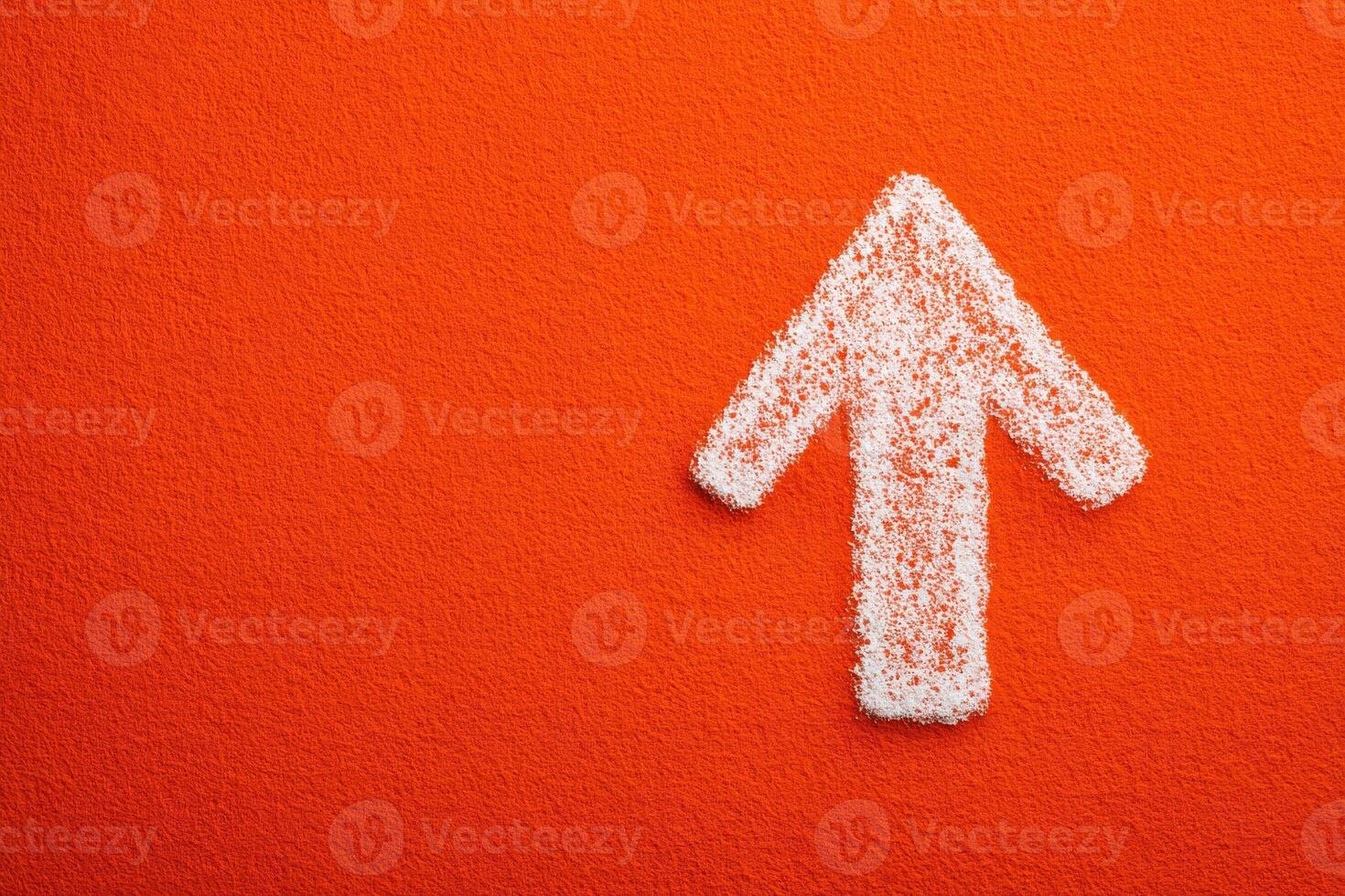 An arrow shaped figure made of white textured material is prominently displayed against a bright orange background. The contrasting colors create a striking visual emphasis on direction. photo