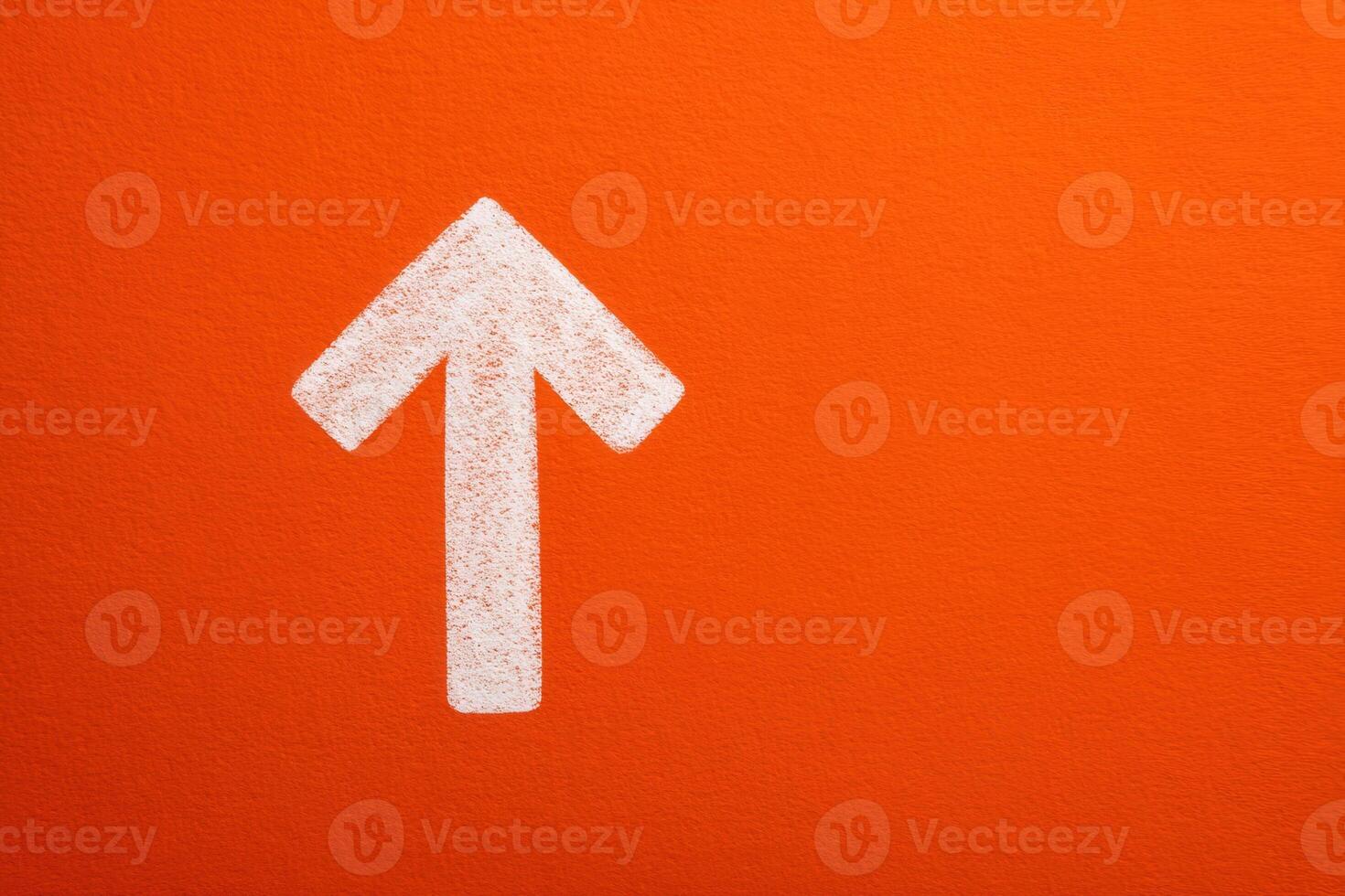 A large white arrow is painted on a vibrant orange wall, directing attention upwards. This striking design element enhances the visual appeal and guides viewers focus. photo