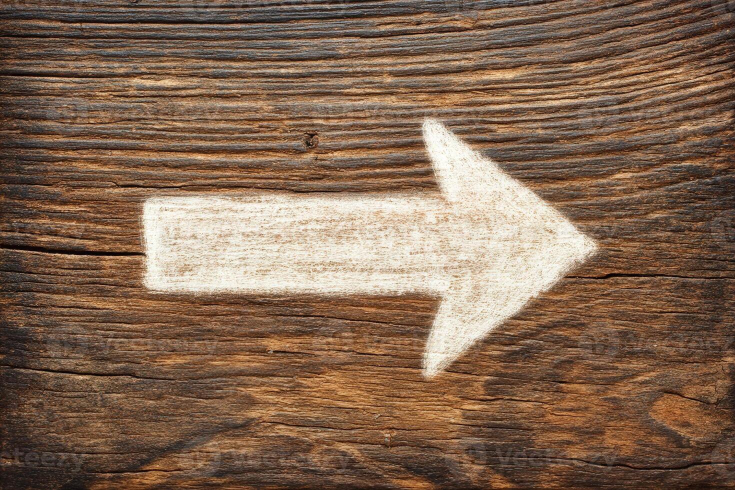 A weathered wooden surface features a white painted arrow pointing to the right. The texture of the wood is rustic, enhancing the arrows visibility and purpose. photo
