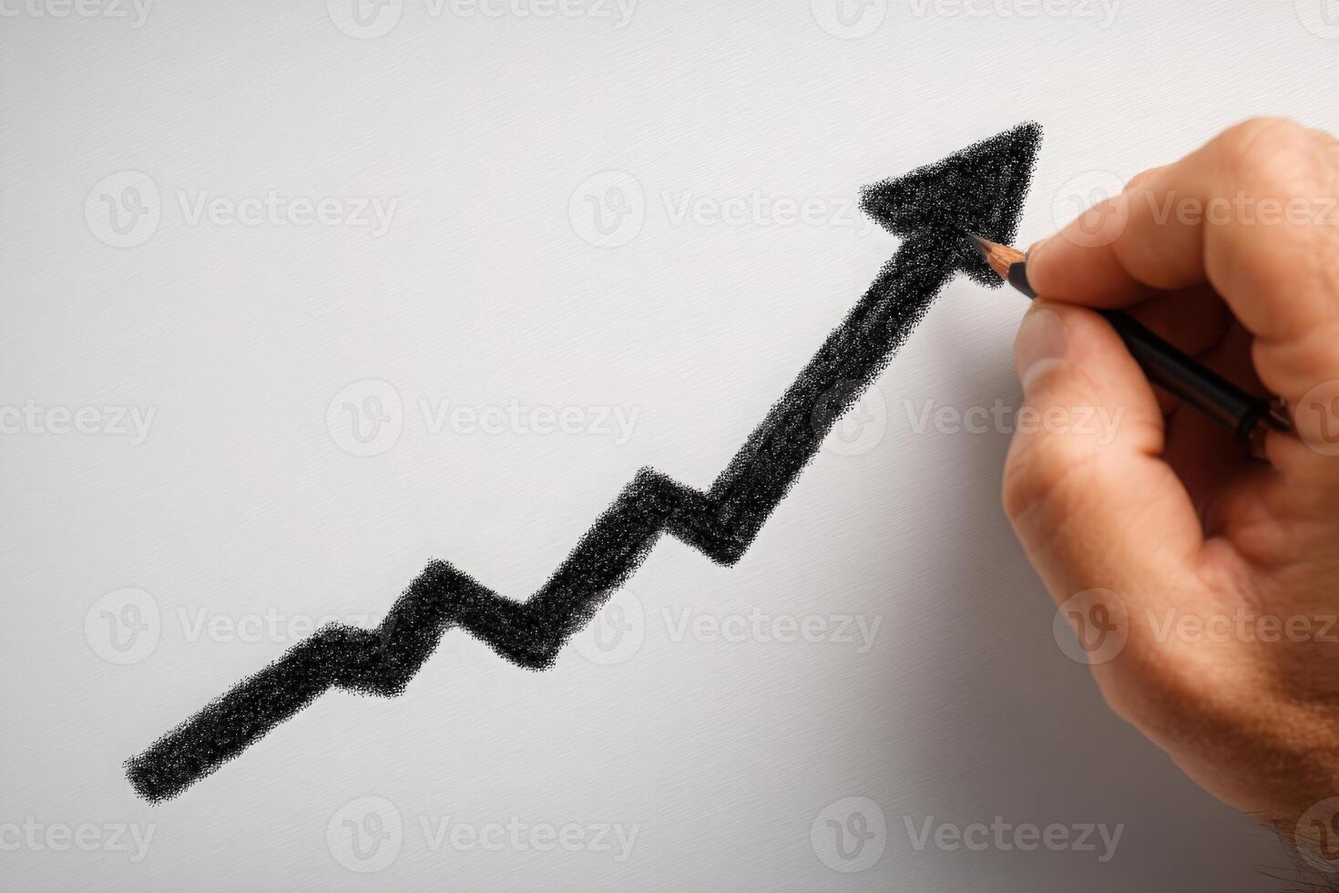 A hand holds a black pencil, sketching a jagged upward trend line on a blank white surface. This represents growth or increasing success, typically associated with financial or business progress. photo