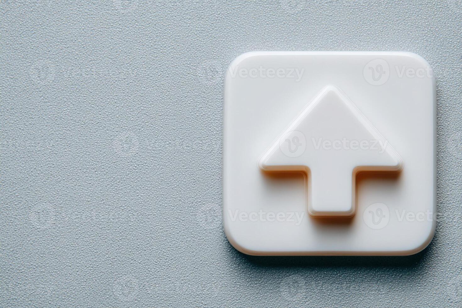 A simple white upload button icon sits prominently on a textured gray surface. The icon features an arrow pointing upwards, indicating a file upload function. photo