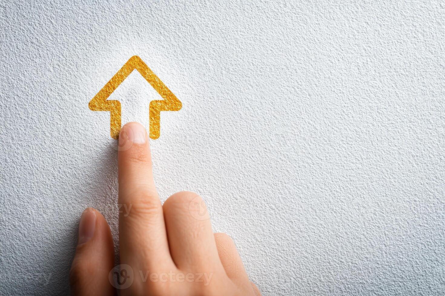 A hand is positioned to touch a stylized golden arrow emblem on a light textured wall. The focus captures the interaction between the human element and the graphic design. photo