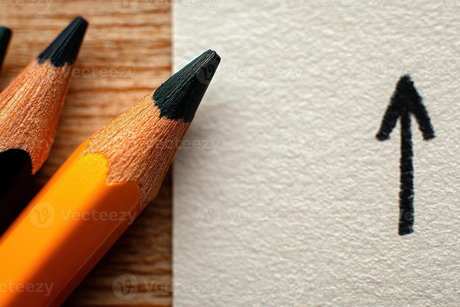 Orange and black pencils rest beside a white sheet of paper featuring a bold upward arrow. The artistic arrangement suggests creativity and encourages upward momentum or progression. photo