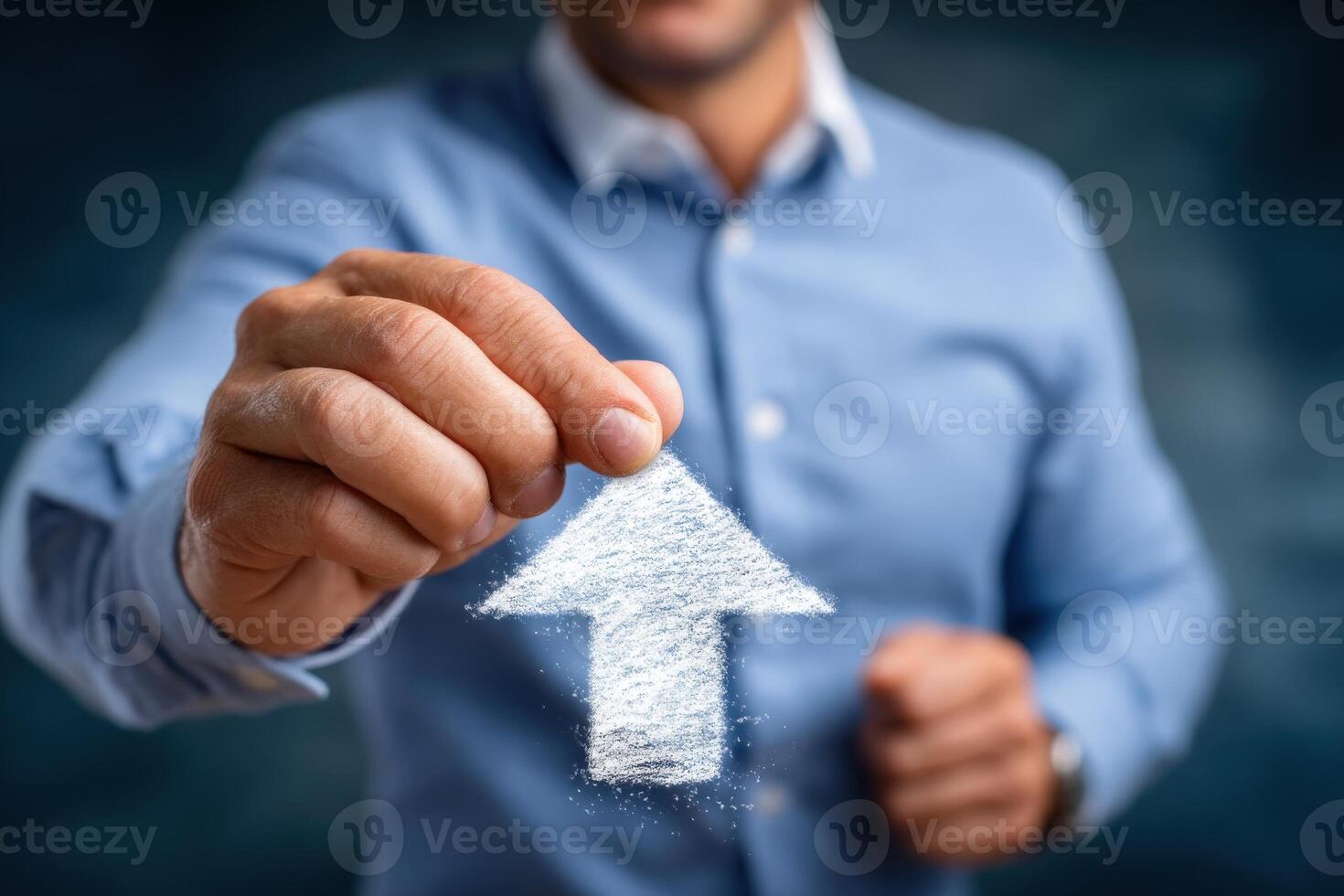 A man in a light blue shirt uses his hand to form an upward arrow with white powder against a blurred blue backdrop. He focuses on the gesture, symbolizing growth or progress. photo