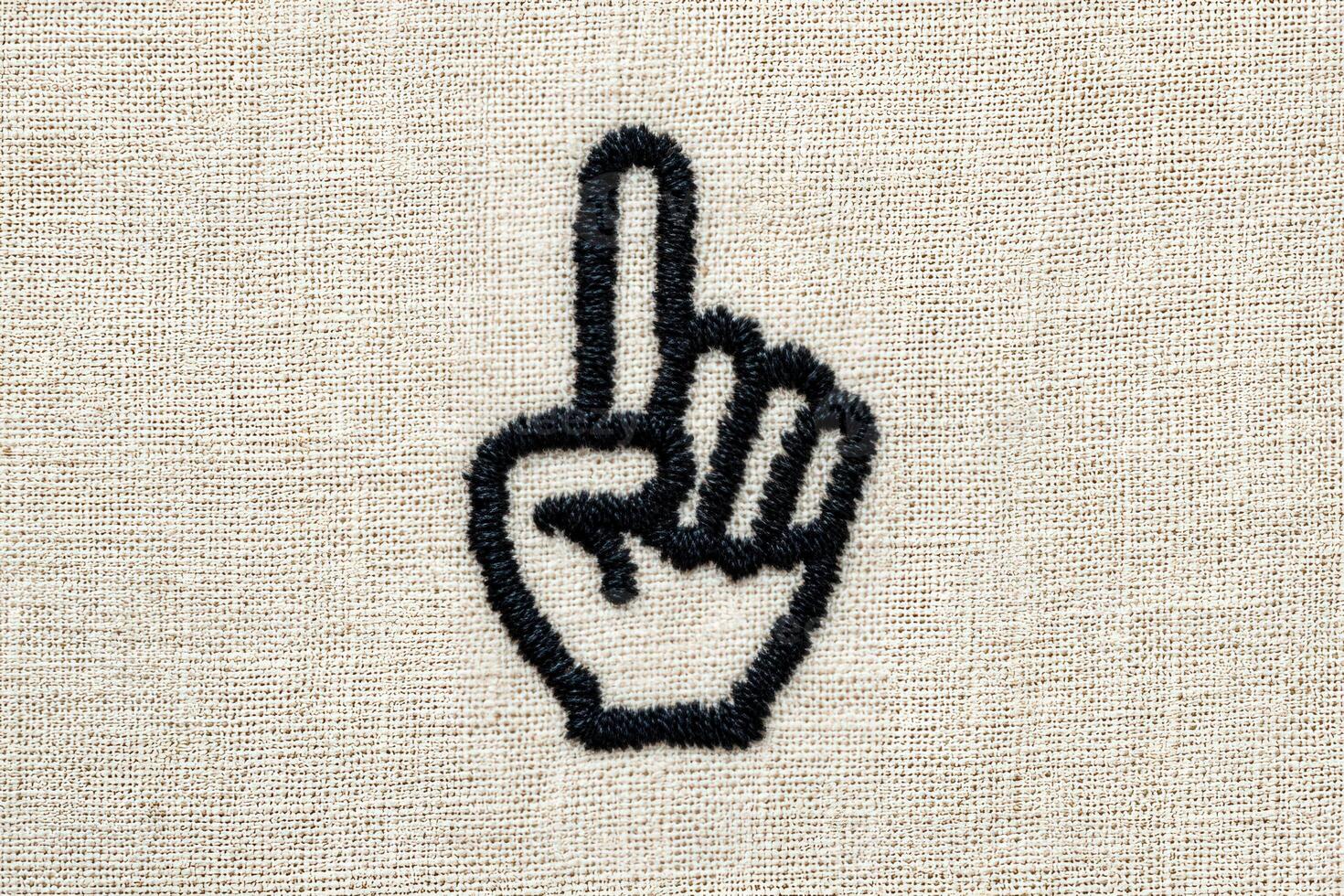 A hand with a raised index finger is embroidered on a beige fabric background. This gesture often signifies asking for attention or pointing out something important. photo