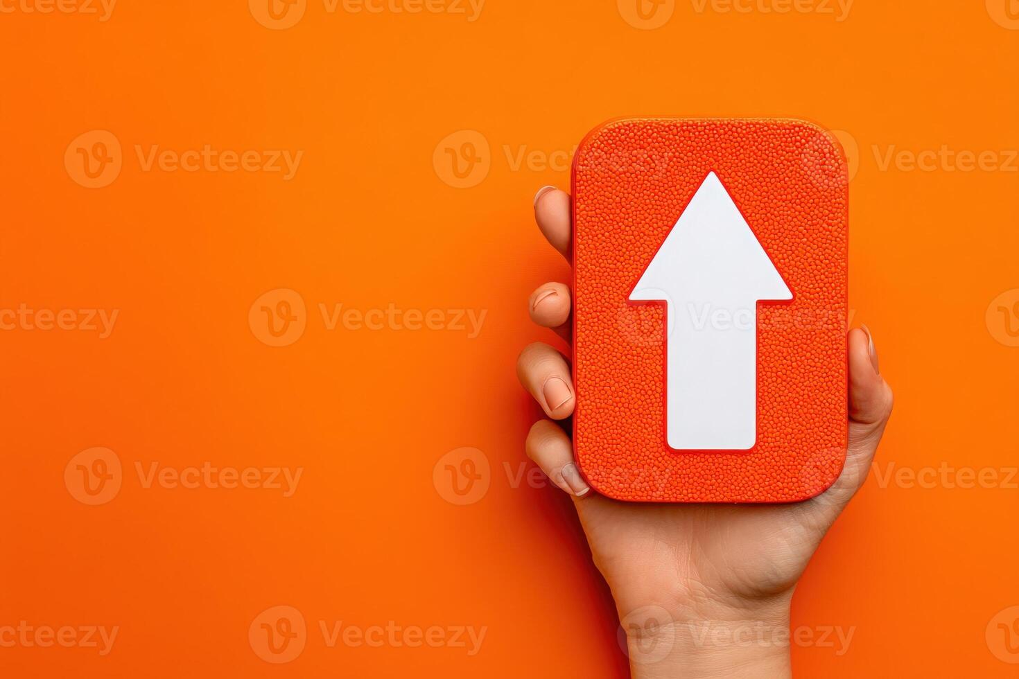 A hand grasps a rectangular orange sign featuring a large white arrow pointing upwards against a vivid orange backdrop. The composition emphasizes clarity and simplicity. photo