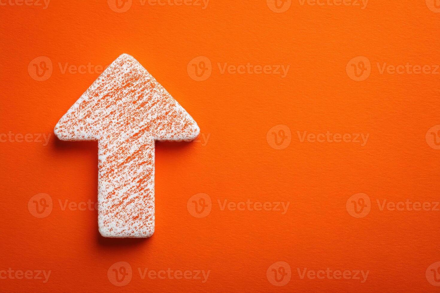 A textured arrow made of white material with orange streaks is positioned on a vibrant orange surface. The arrow points upward, symbolizing direction and growth in a minimalist setting. photo
