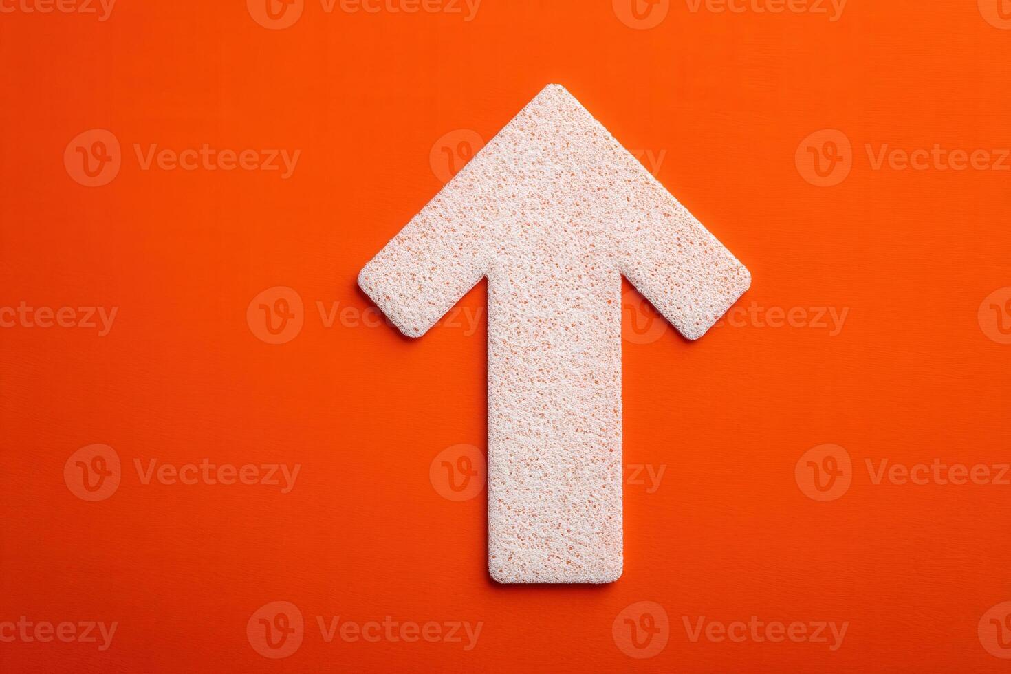 A large, textured arrow points upwards against a solid orange background, showcasing a minimalist design. The arrows surface has a subtle grain, adding depth to the composition. photo