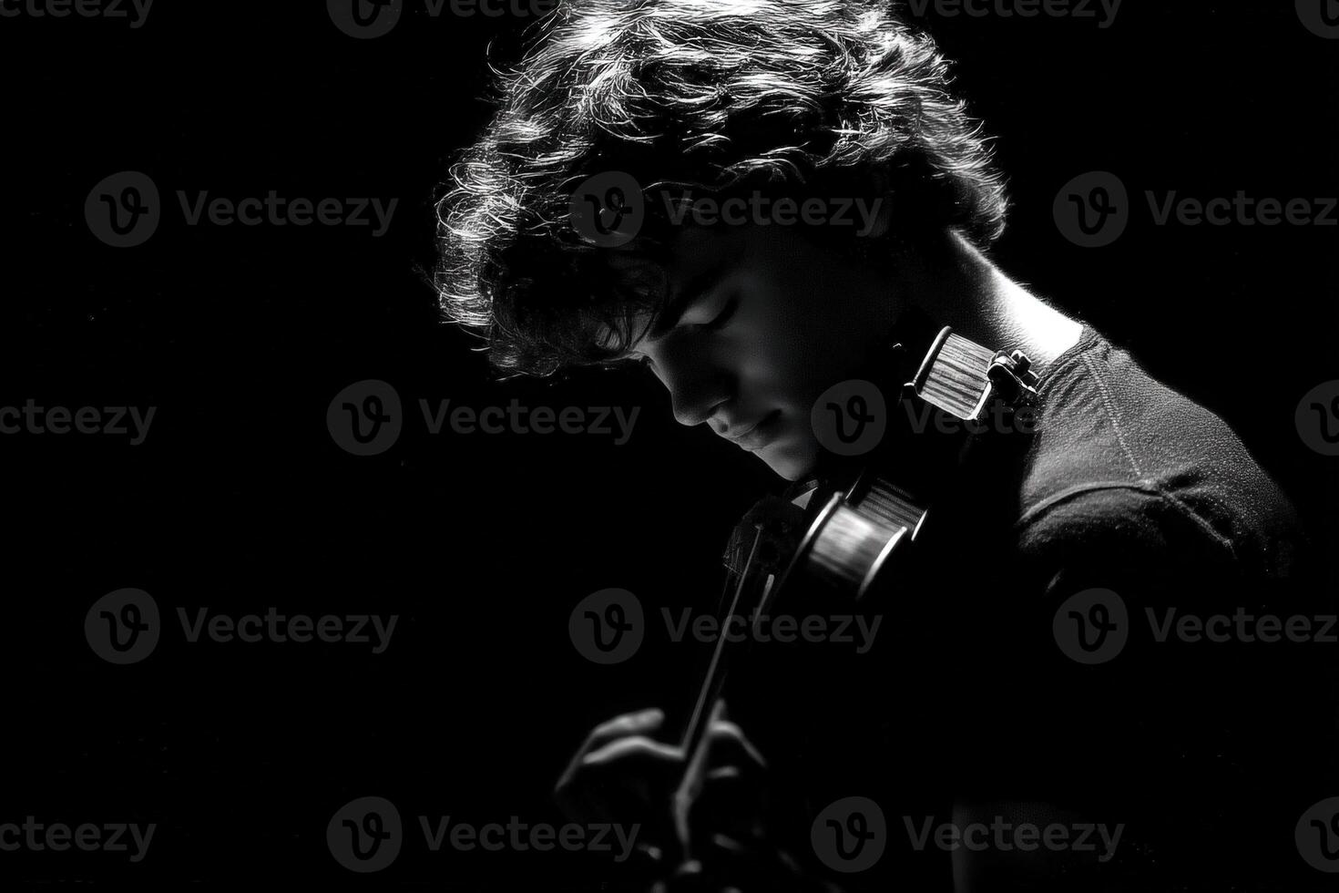 A young musician, with curly hair, deeply focuses on playing the violin. Soft light highlights his profile against a dark background, capturing a moment of artistic dedication and passion. photo
