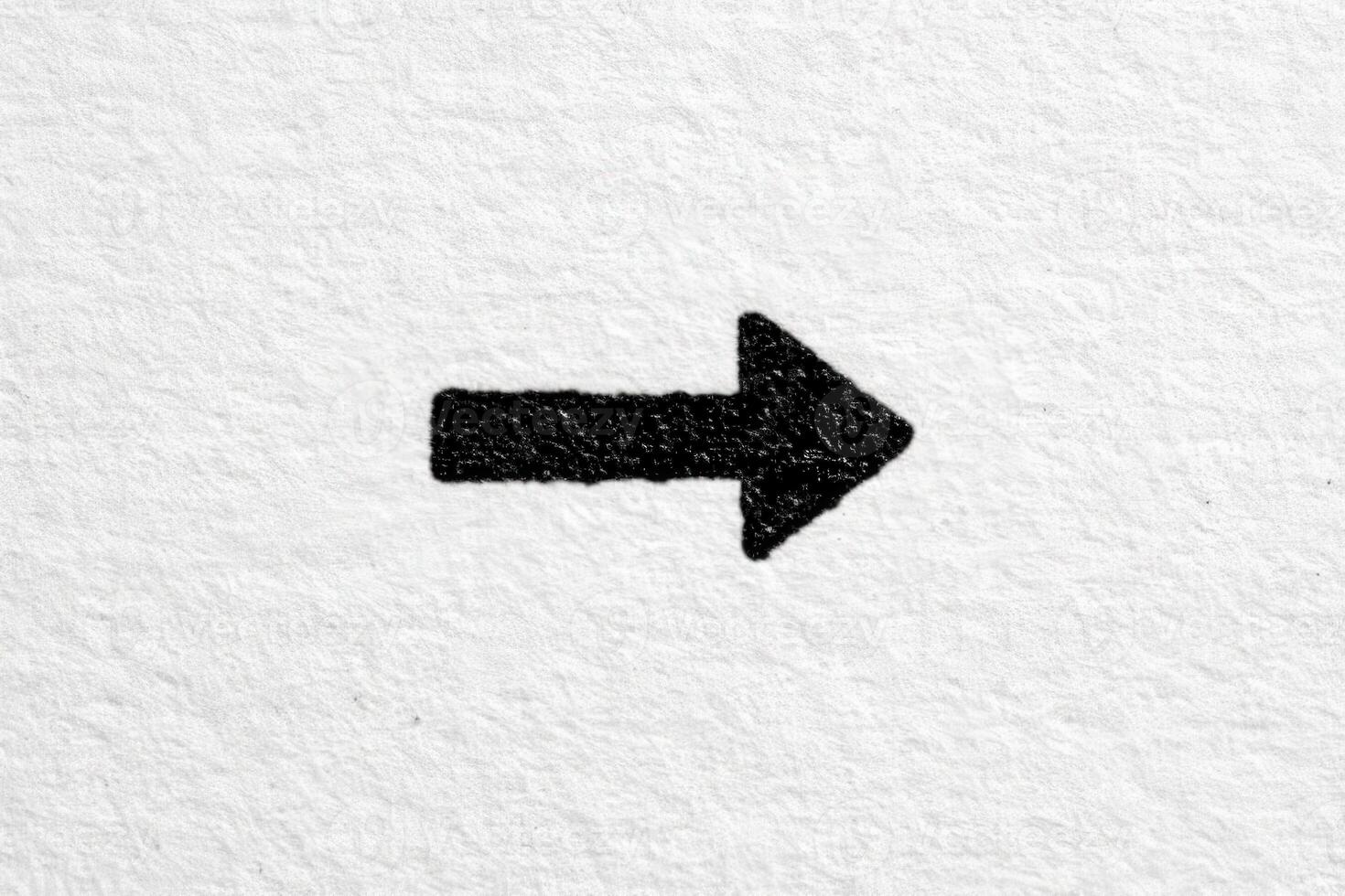 A bold black arrow is drawn on a textured white paper, clearly indicating a rightward direction. The contrast between the black ink and white background highlights the arrows shape and intention. photo