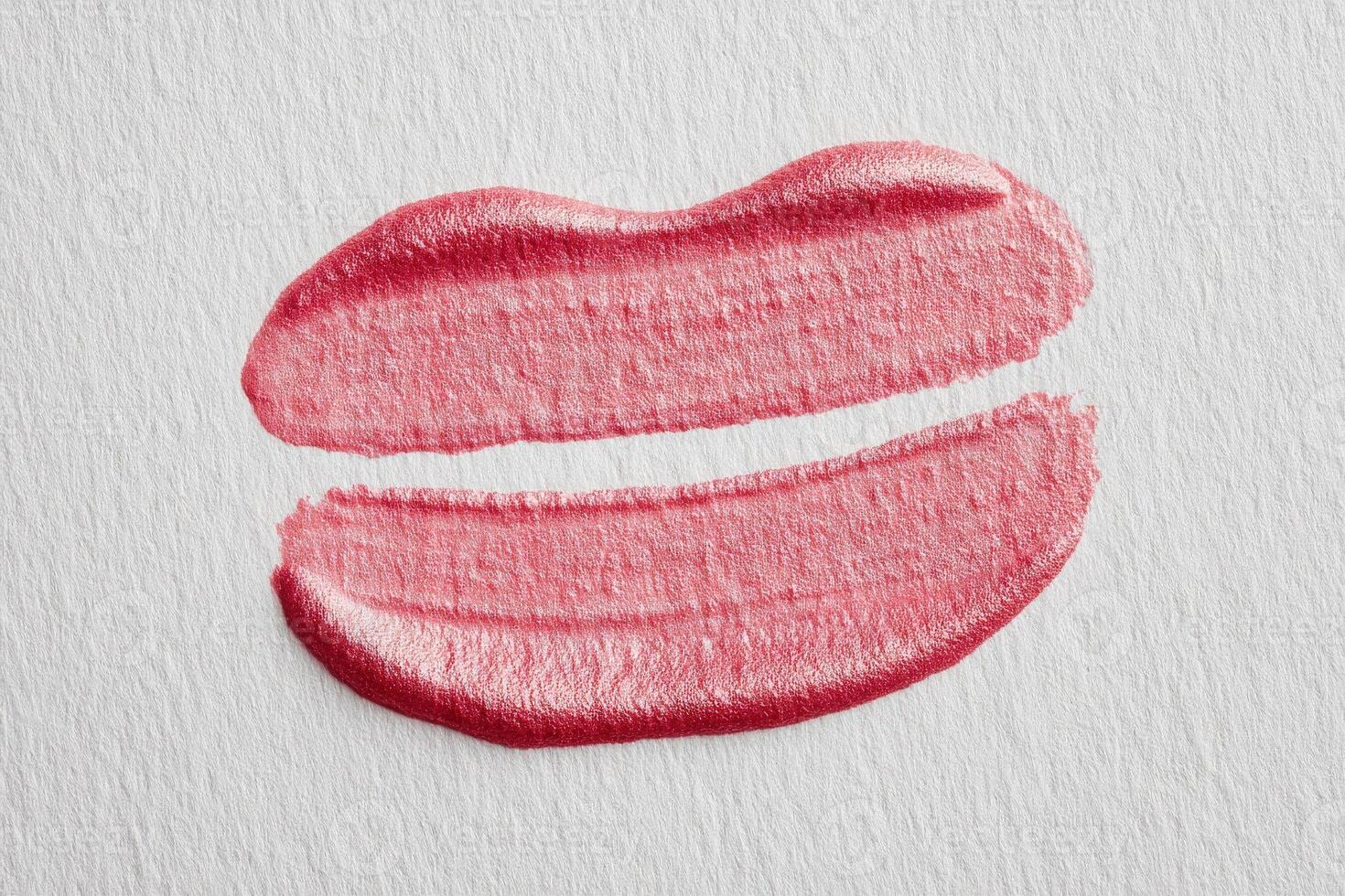 A kiss mark in soft pink lipstick is displayed on lightly textured white paper, showcasing two well-defined lip impressions. The natural lighting highlights the creamy texture. photo