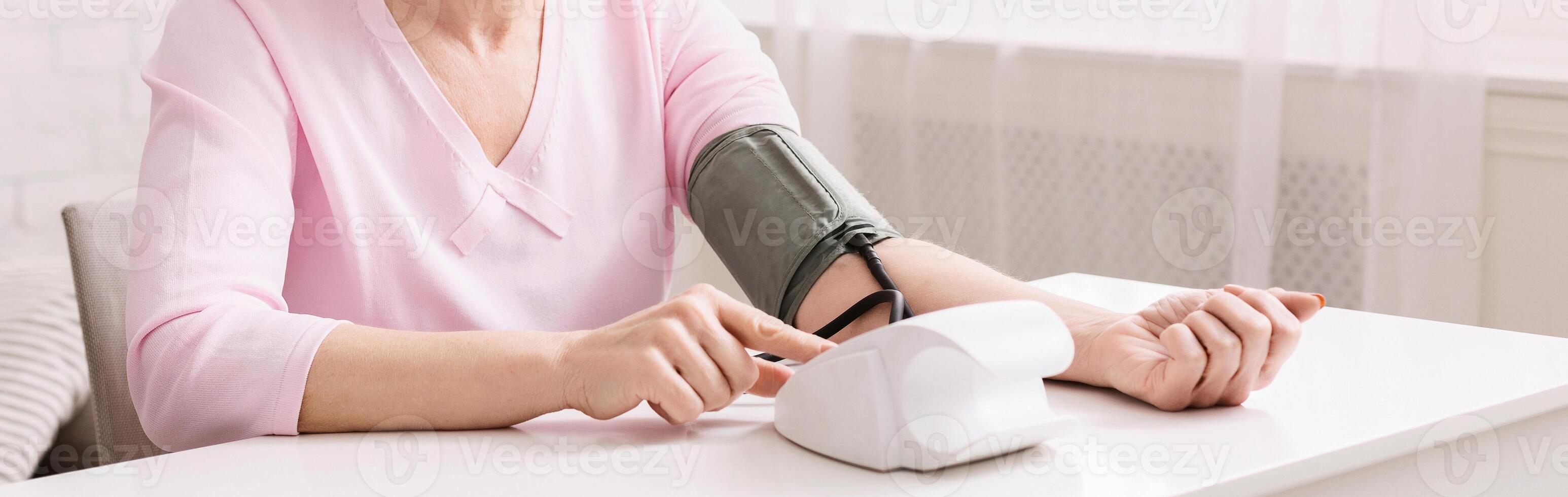 Mature woman with hypertension measuring blood pressure herself, panorama with empty space photo