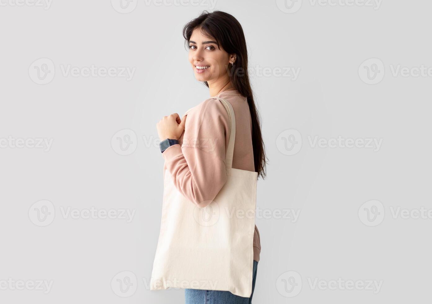 Environmental Protection. Portrait of smiling woman standing with blank canvas tote bag, free copy space for design mockup, isolated on studio background wall. Handmade female shopping bag photo