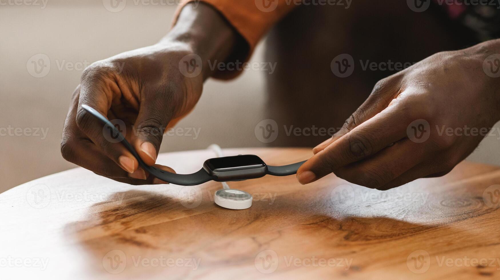 African american man putting smartwatch for charging on wireless charger on table, closeup, cropped. New modern technology concept photo