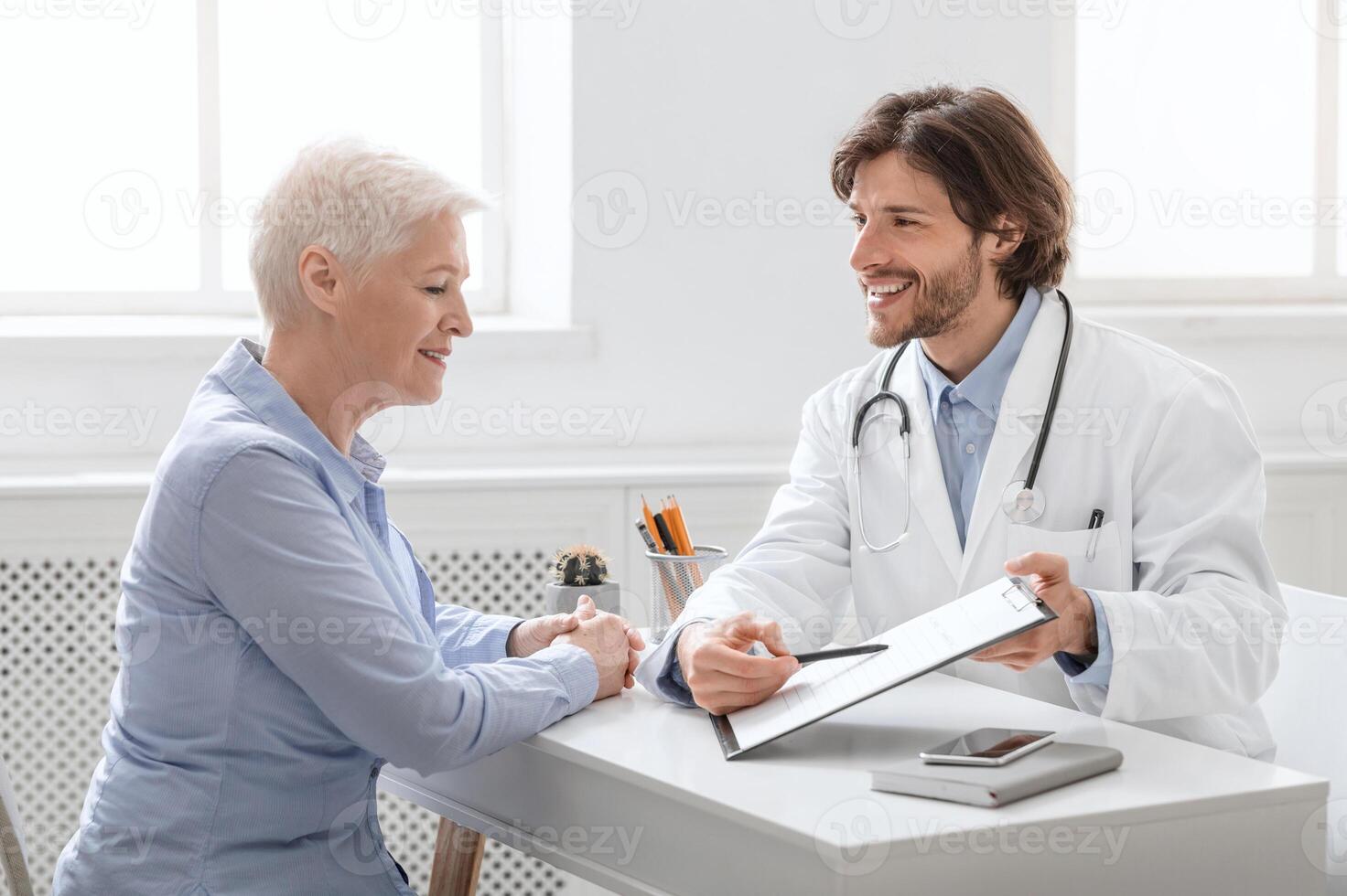 Successful treatment. Cheerful doctor showing good test results to senior patient at hospital, side view photo