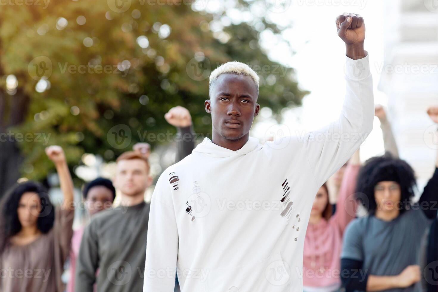 Black man leading international group of students, raising fist up and looking at camera. African american man leader standing in front of multiracial group of protestors on the street, copy space photo
