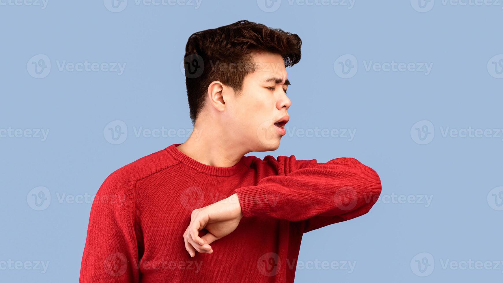Stop Virus And Germs Spreading Concept. Closeup portrait of asian guy in sweater showing correct way of sneezing, coughing in his elbow isolated over studio backgound, banner, panorama, copy space photo