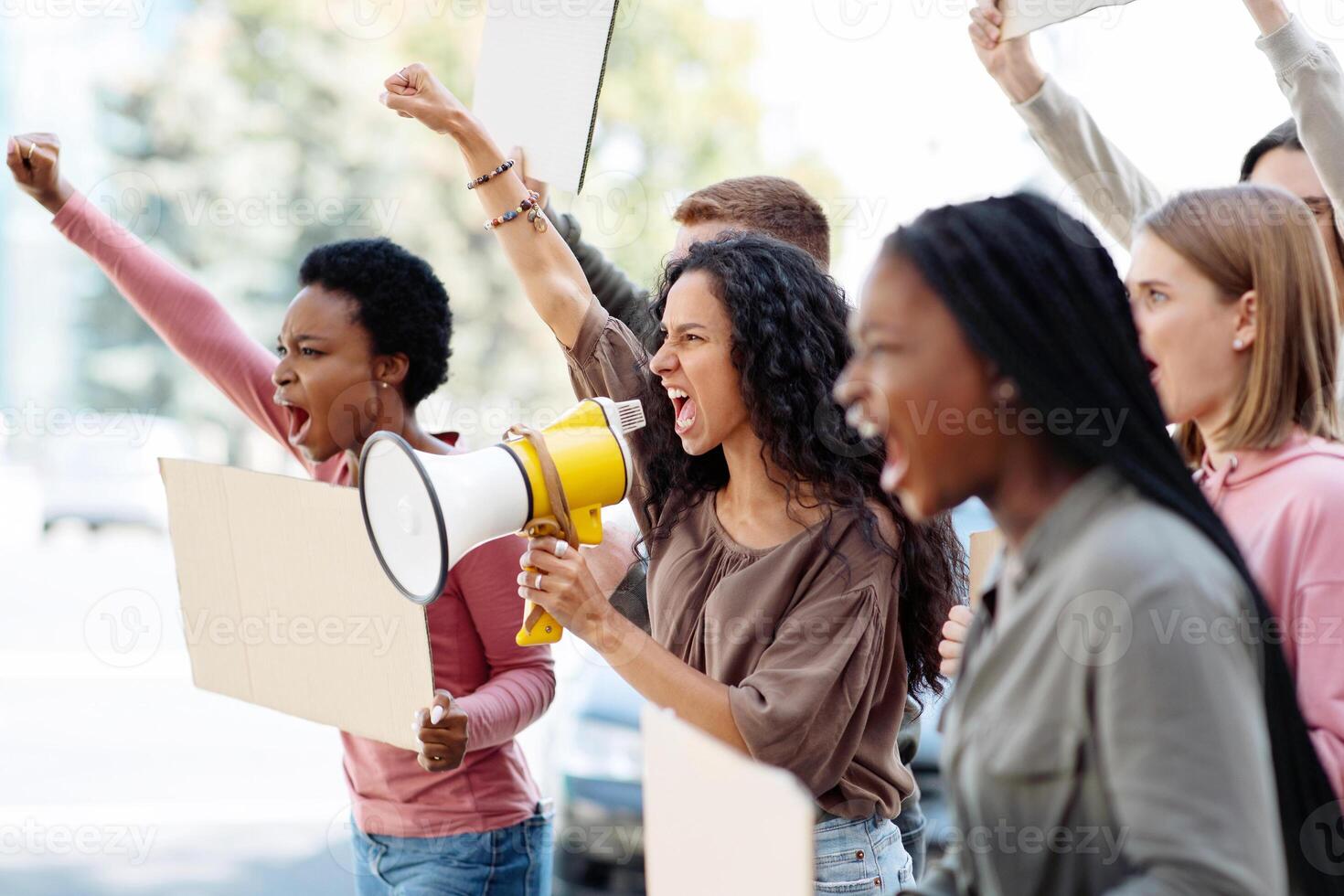 Active young people making strike on the street, using loudspeaker, holding blank placards, side view, copy space. International group of angree demonstrators fighting against war photo