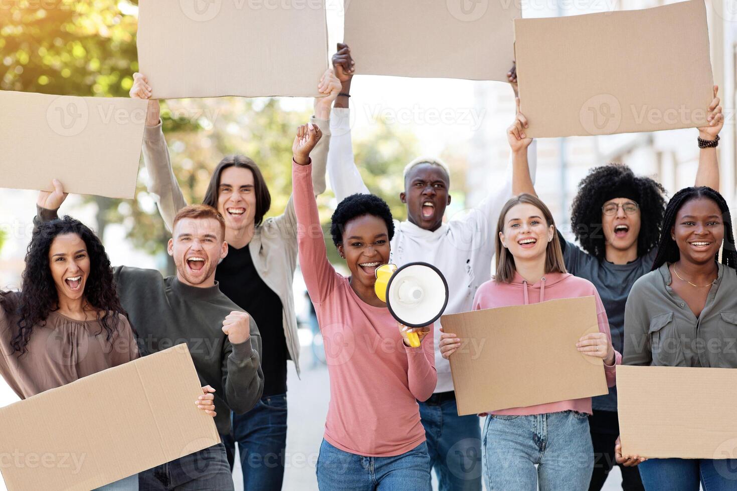 Black motivated lady with loudspeaker leading international group of strikers, demonstrators yelling slogans and holding empty placards, walking by street. Strike, demonstration, protest concept photo