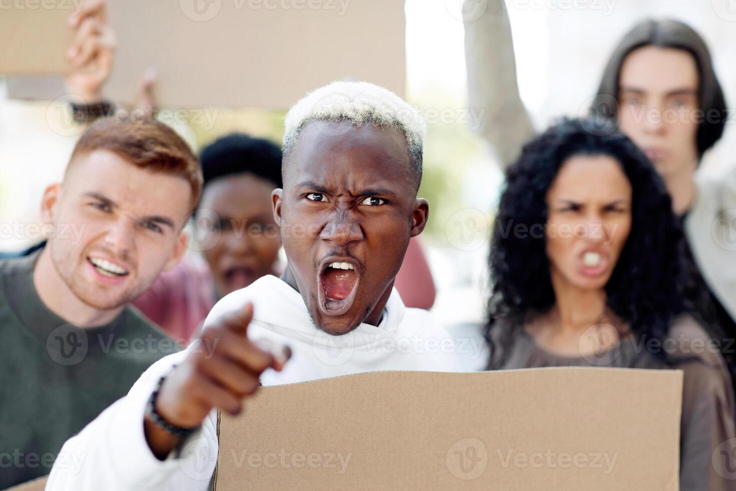 Mutiracial group of demonstrators striking on the street, holding blank placards, pointing at camera. International group of demonstrators fighting against racism, walking by city, chanting slogans photo