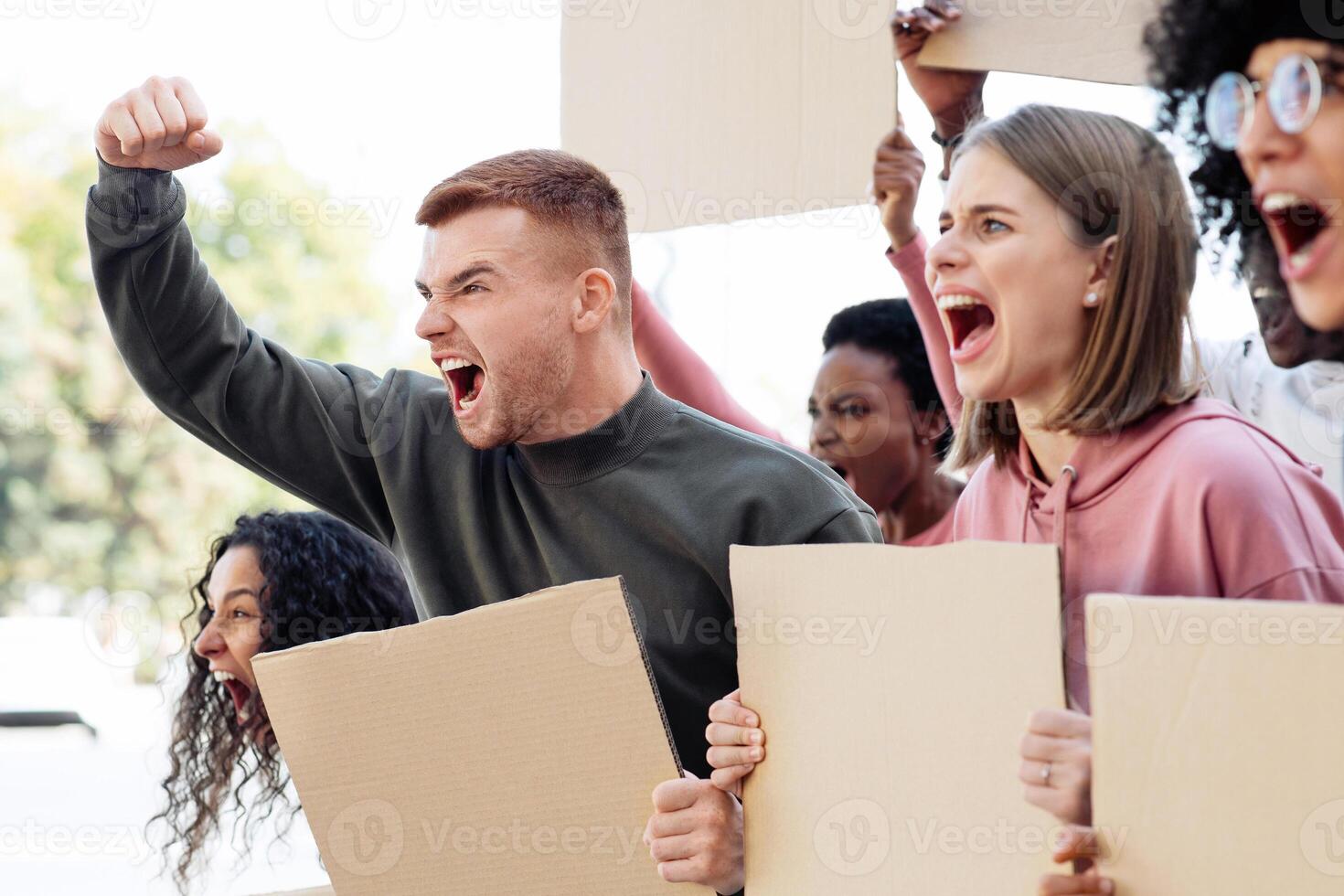 Closeup of international young group of motivated demonstrators with empty placards on the street. Strikers with blank slogan boards yelling and raising fists up, fighting for human rights, copy space photo