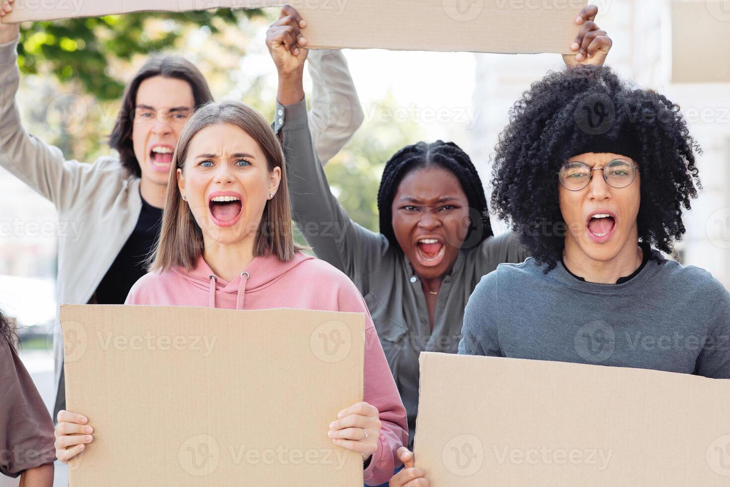 Furious mutiracial group of demonstrators protesting on the street, holding blank placards. International group of demonstrators fighting against racism, walking by the city, chanting slogans, closeup photo