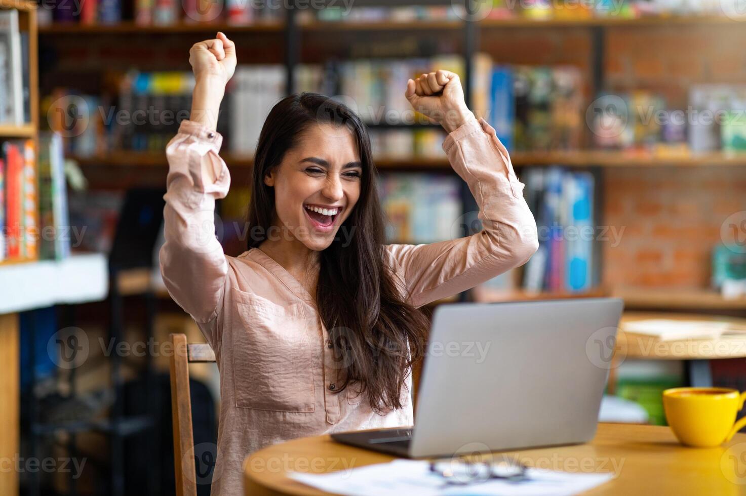 Lucky day. Emotional latin woman celebrating success in front of laptop at cafe, clenching fists, screaming and exclaining with joy. Overjoyed lady working distantly, free space photo