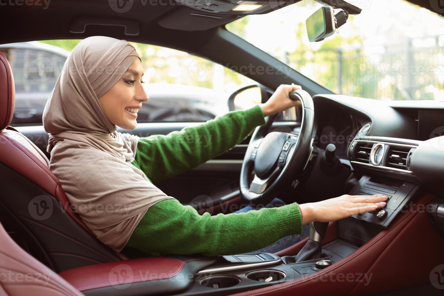 Test Drive Concept. Profile Portrait Of Islamic Lady In Headscarf Driving Car And Turning On Radio Music, Checking Automobile Options, Pushing Button On Functional Panel In Her Luxury Vehicle photo